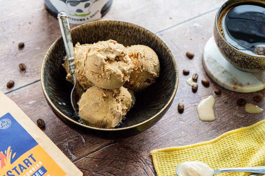 Scoops of Marshfield x TrueStart True Coffee ice cream in a bowl beside a cup of coffee